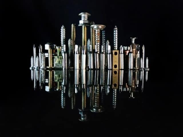 Foto profissional de estúdio com vários tipos de parafusos e fixadores organizados sobre uma superfície espelhada com fundo preto, representando a Veppel, RJ