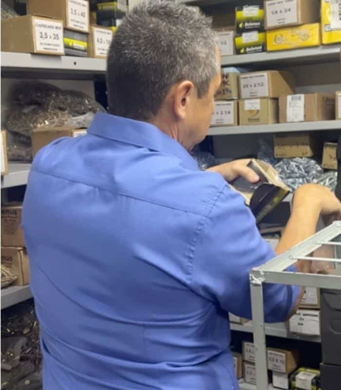 O proprietário Valmir buscando um item específico nas prateleiras de parafusos da Veppel, mostrando o vasto estoque da empresa no Rio de Janeiro.