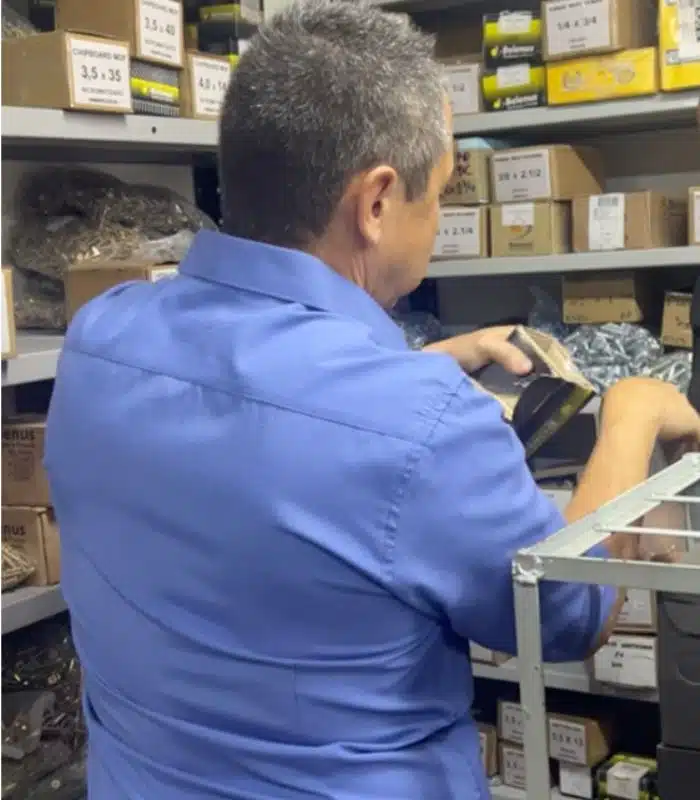 O proprietário Valmir buscando um item específico nas prateleiras de parafusos da Veppel, mostrando o vasto estoque da empresa no Rio de Janeiro.